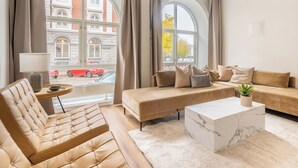 Ett modernt vardagsrum med en soffa, fåtölj och soffbord, stora fönster med gardiner och utsikt över en röd bil som står utanför.