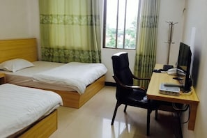 Habitación de hotel con dos camas individuales, un escritorio con ordenador, una silla y una ventana con cortinas.