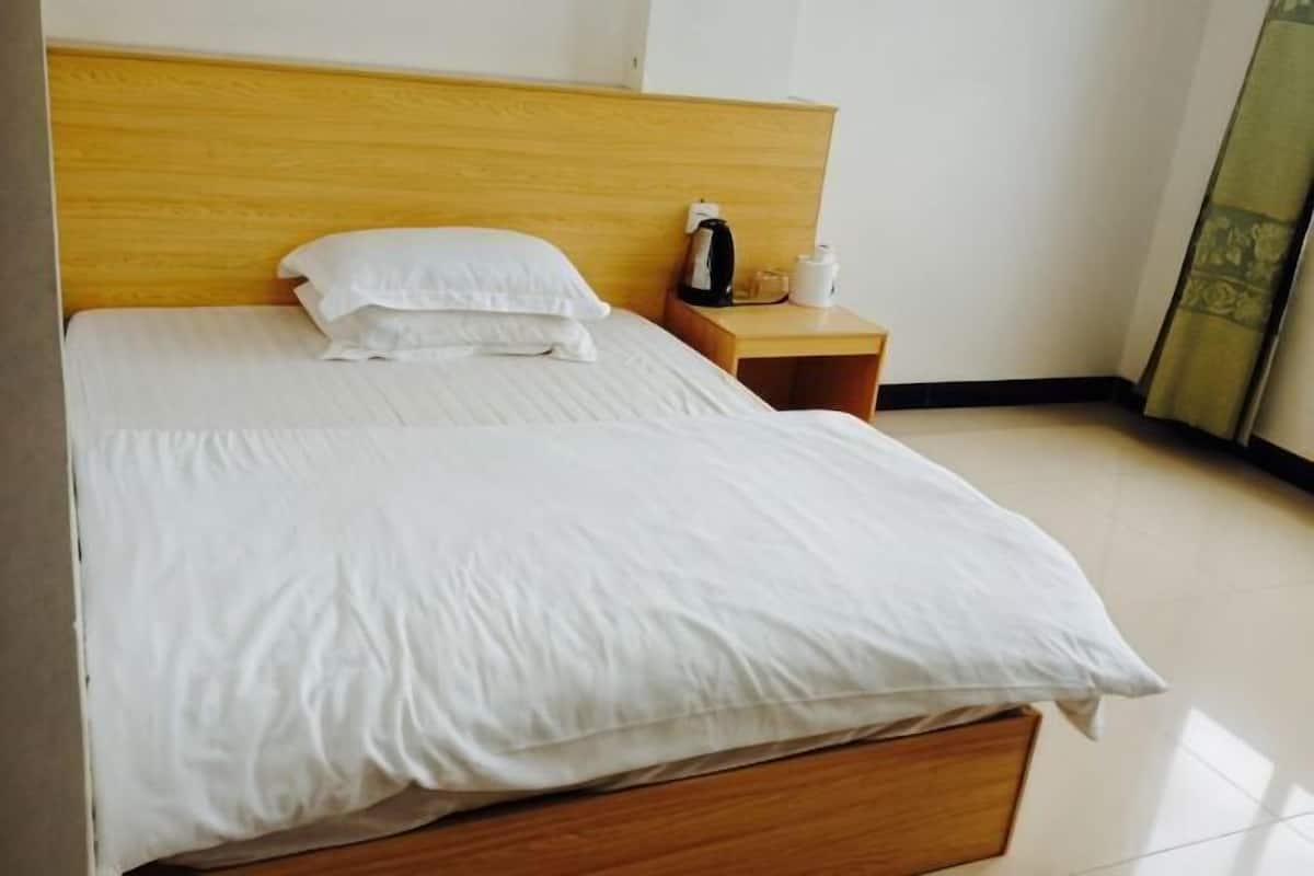 Uma cama bem arrumada com lençóis brancos, uma cabeceira de madeira, uma mesinha de cabeceira com uma cafeteira e vista para o interior do quarto.