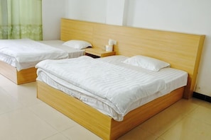 Een hotelkamer met twee houten bedden, wit beddengoed, een nachtkastje met een lamp en een groen gordijn.