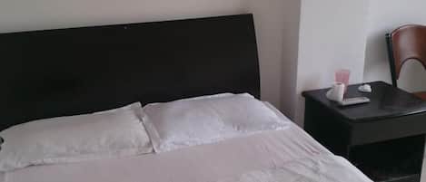 A neatly made bed with white linens, a dark headboard, and a small bedside table with a tissue box and a cup.