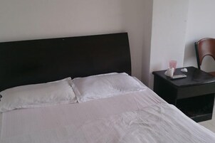 A neatly made bed with white linens, a dark headboard, and a small bedside table with a tissue box and a cup.