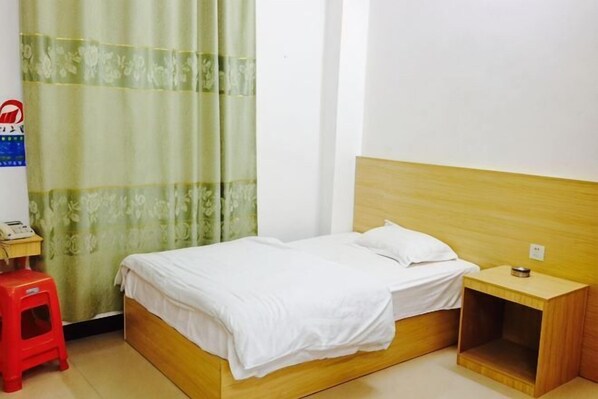 A single bed with a wooden headboard, a nightstand, a red stool, and a green curtain.
