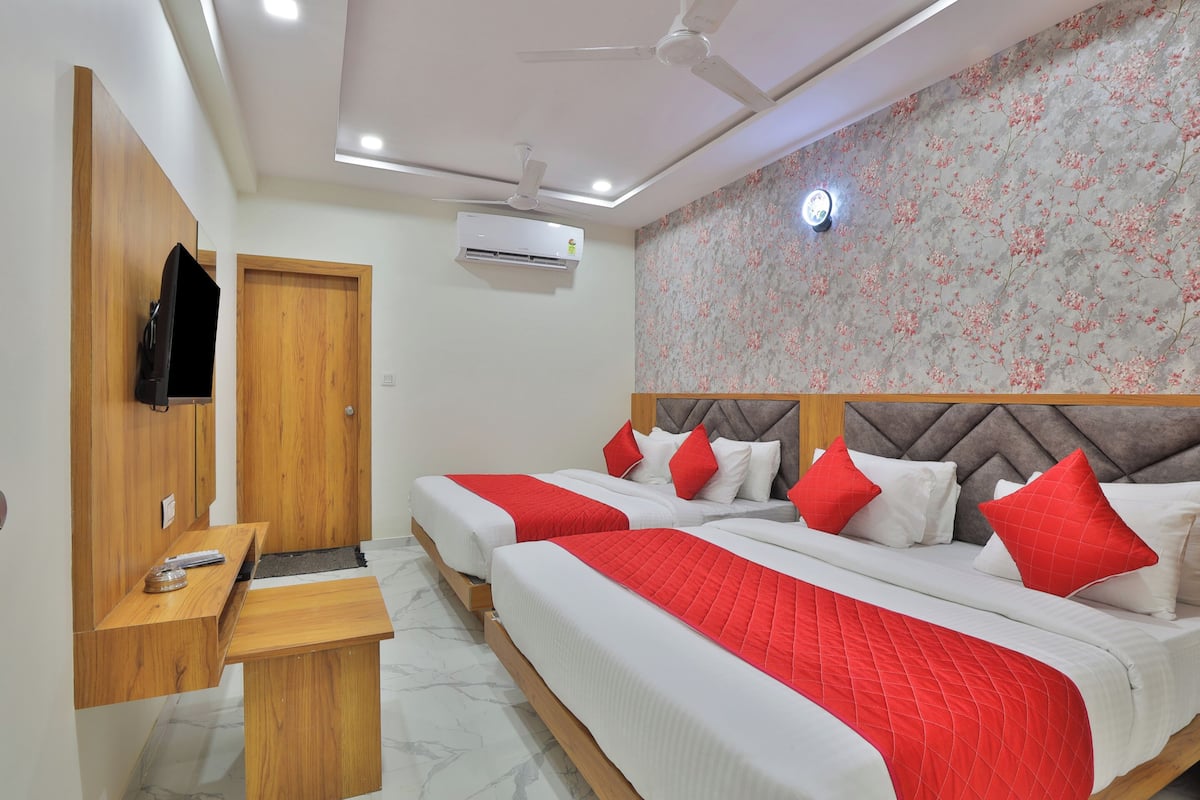 A hotel room with two beds, a wooden desk, a TV, and an air conditioning unit.