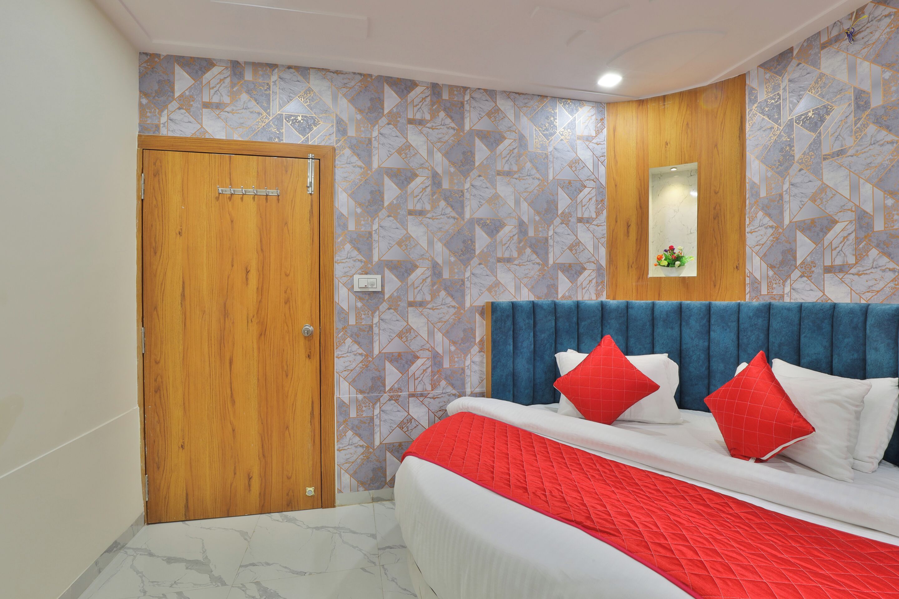 A bedroom with a wooden door, a bed with a blue headboard, and patterned wallpaper.