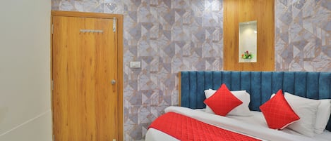 A bedroom with a wooden door, a bed with a blue headboard, and patterned wallpaper.