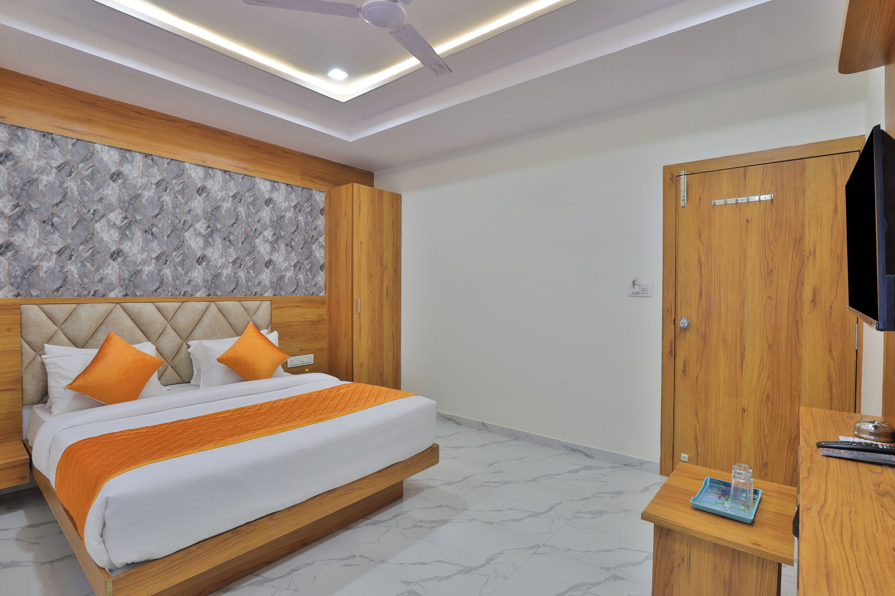 A modern hotel room with a large bed, wooden headboard, and a built-in TV.