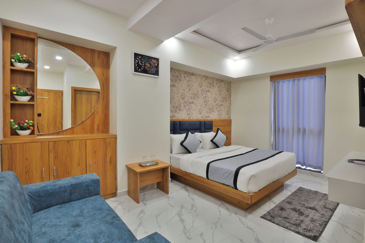 A modern bedroom with a wooden wardrobe, a bed with a headboard, a small bedside table, a blue sofa, and a large mirror.