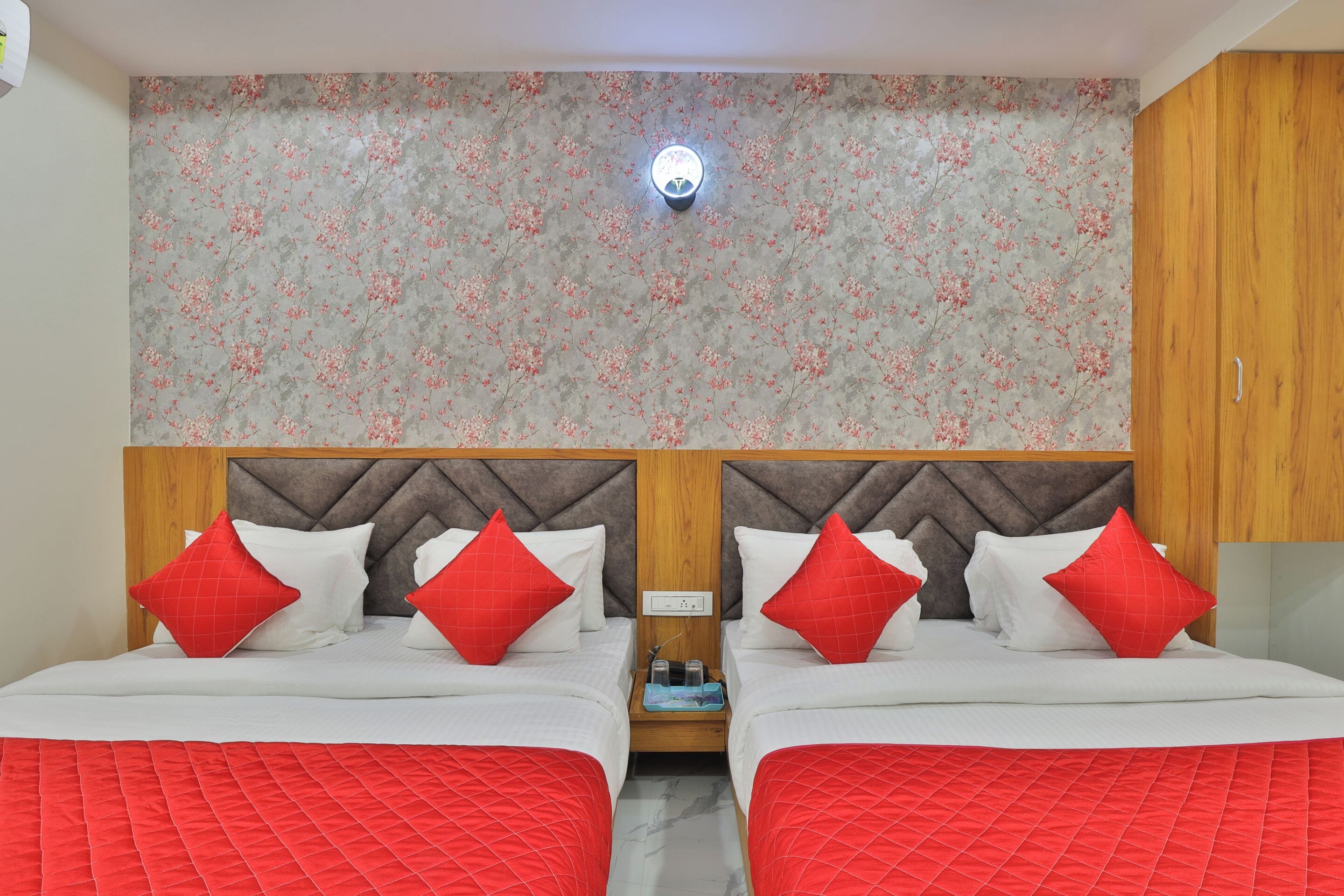 A double bed with red and white bedding, a wooden headboard, and a floral wallpaper design.
