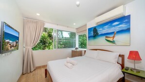 A bedroom with a bed, a nightstand, a red lamp, a painting of a boat on a beach, and a window with curtains. - Karon ButterFly Apartment E107 for 3  (Karon)