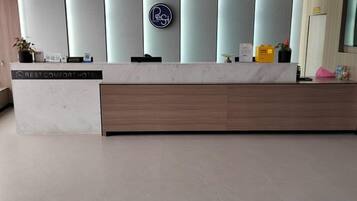 A hotel reception desk with a marble top, a wooden panel, and a vertical sign with a logo.