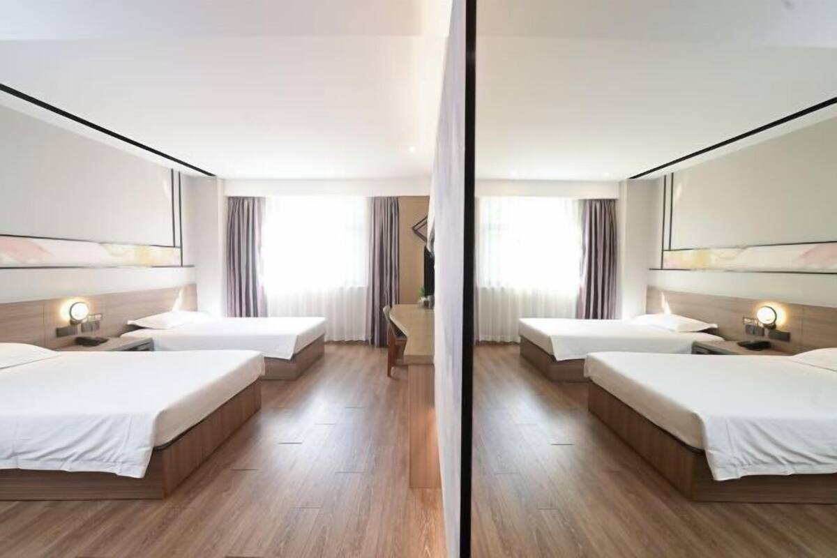 A mirrored hotel room with two beds, wooden flooring, and a central seating area.