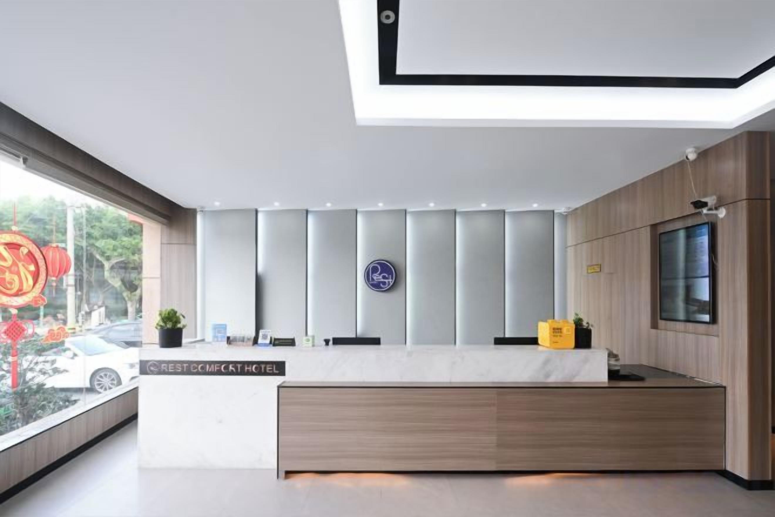Un espace d’accueil d’hôtel au design moderne, comprenant un comptoir d’accueil, un écran numérique et une fenêtre donnant sur la rue.