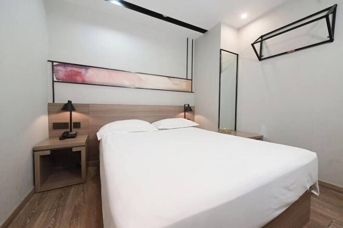 A modern bedroom with a large bed, bedside tables, a wall-mounted artwork, and a mirror.