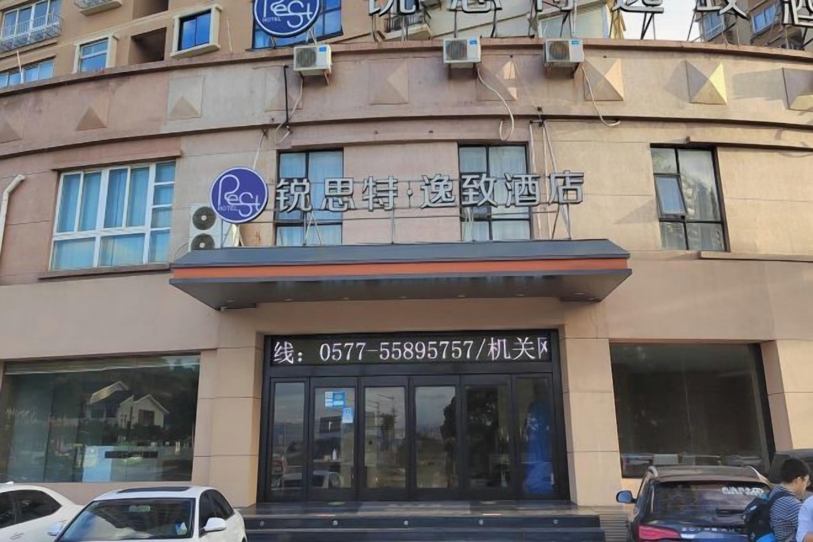 A building with a sign for a hotel. There are windows on the facade, and a car is parked in front.