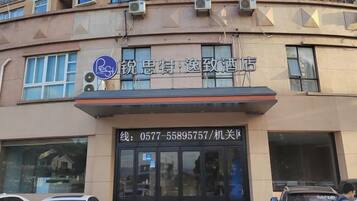 A building with a sign for a hotel. There are windows on the facade, and a car is parked in front.