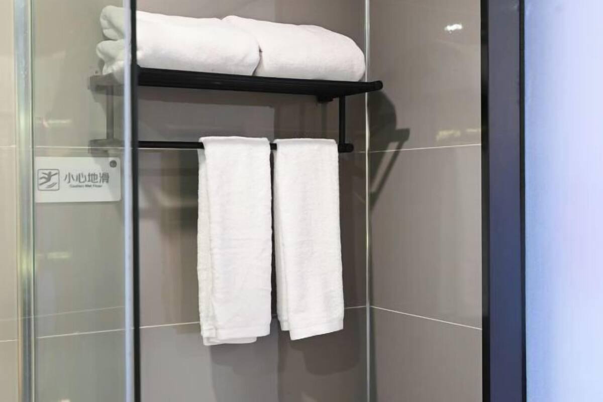 A glass shower enclosure with a black towel rack holding two white towels.