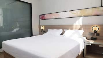 Quarto de hotel moderno com cama grande, mesas de cabeceira e uma janela ampla.