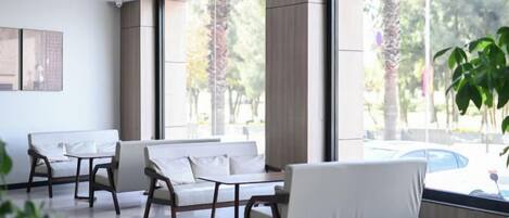 A modern hotel lobby with a seating area, large windows, and a view of the outdoors.