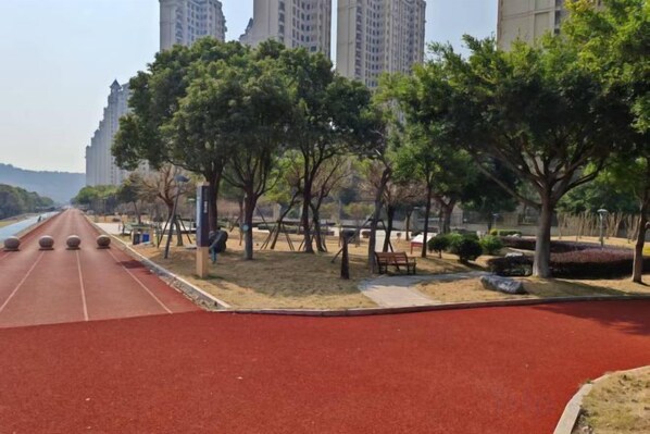 Una pista de atletismo roja con árboles y bancos, rodeada de edificios.