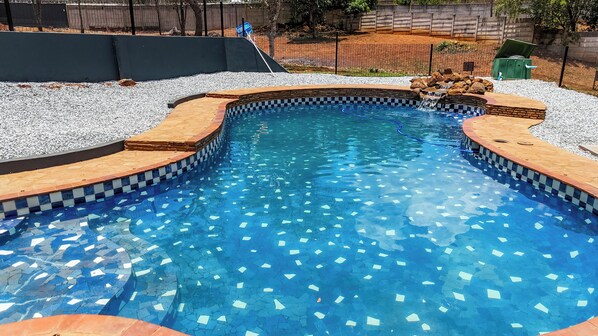 A swimming pool with a mosaic tile border and a small waterfall feature. - Casa Favorita (Harare)