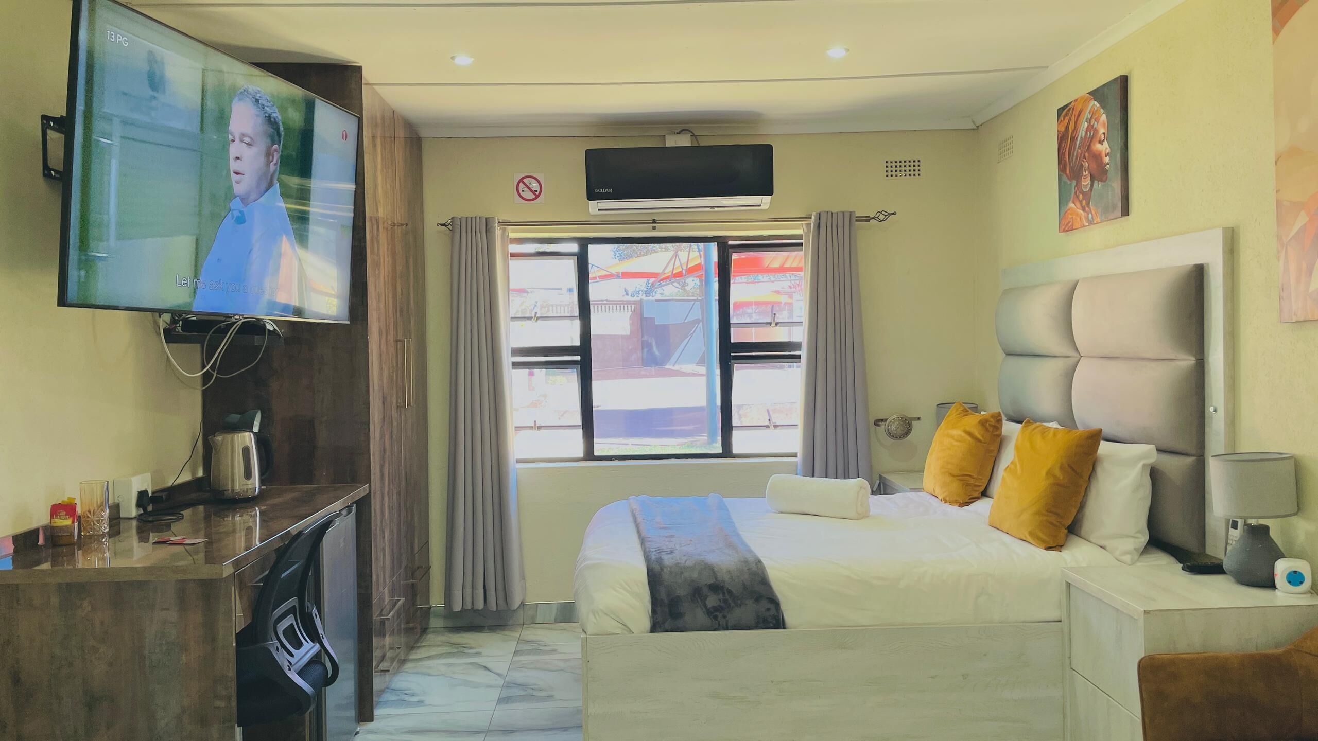 A hotel room with a bed, a TV mounted on the wall, a window with curtains, and a ceiling fan.