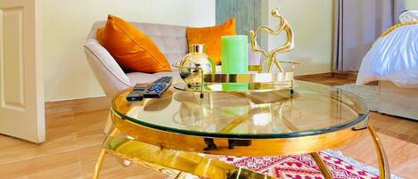 Una sala moderna con una mesa de centro de vidrio, un sofá con cojines naranjas y una alfombra estampada.