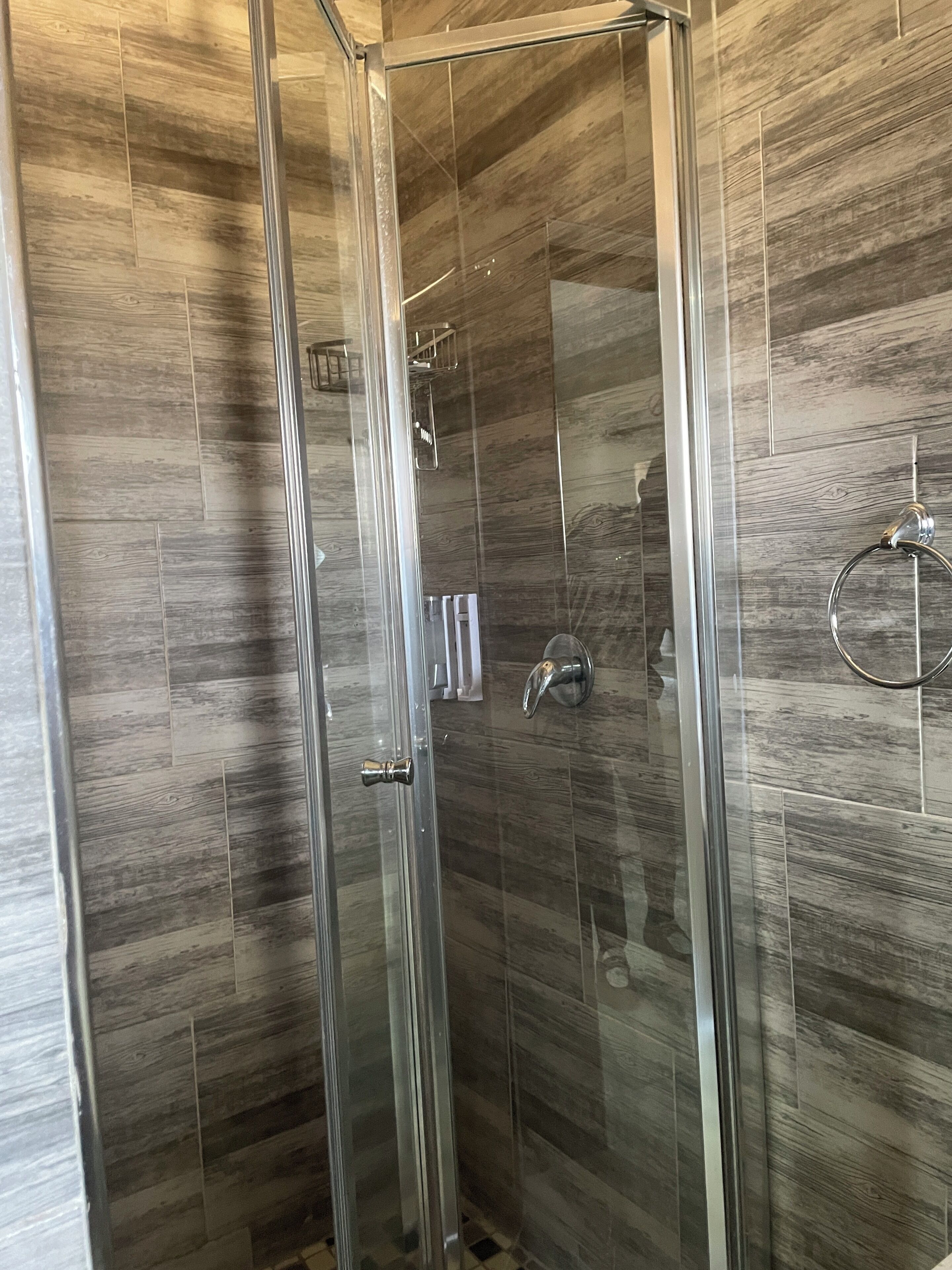 A glass-enclosed shower with a wooden panel wall.