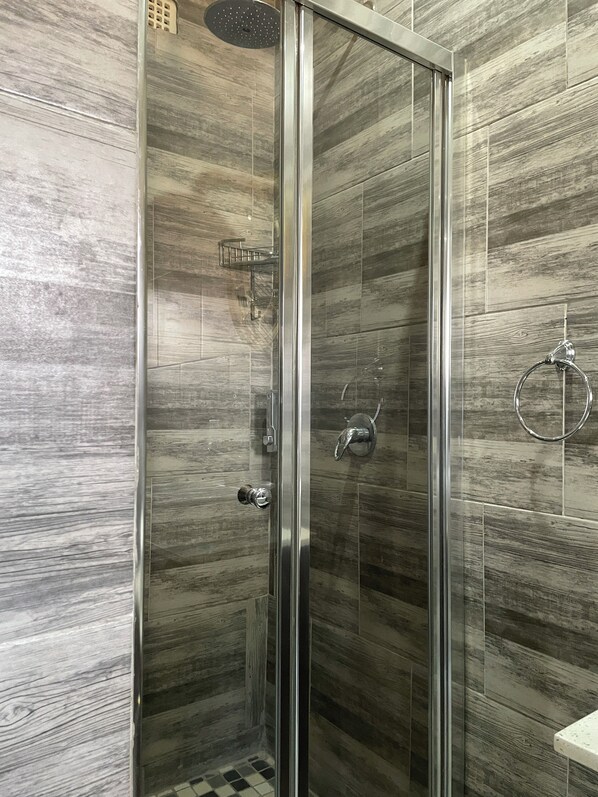 A glass-enclosed shower with a wooden panel wall, a showerhead, and a towel ring. - Casa Favorita (Harare)