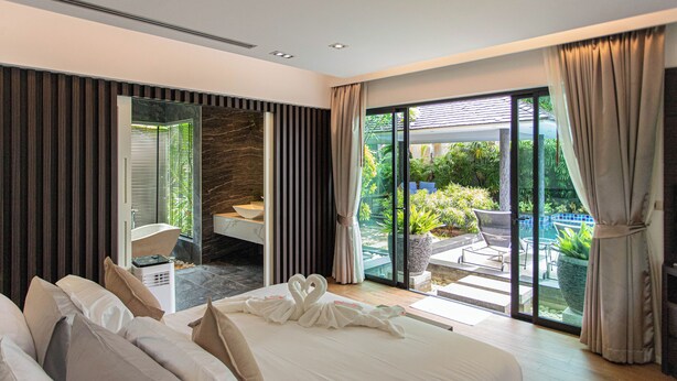 A modern hotel room with a large bed, a sitting area with a view of the garden, and a bathroom with a bathtub. - Tropical Haven 4 Bedroom Pool Villa (Choeng Thale)