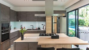 A modern kitchen with a central island, built-in appliances, and a view of a backyard. - Tropical Haven 4 Bedroom Pool Villa (Choeng Thale)