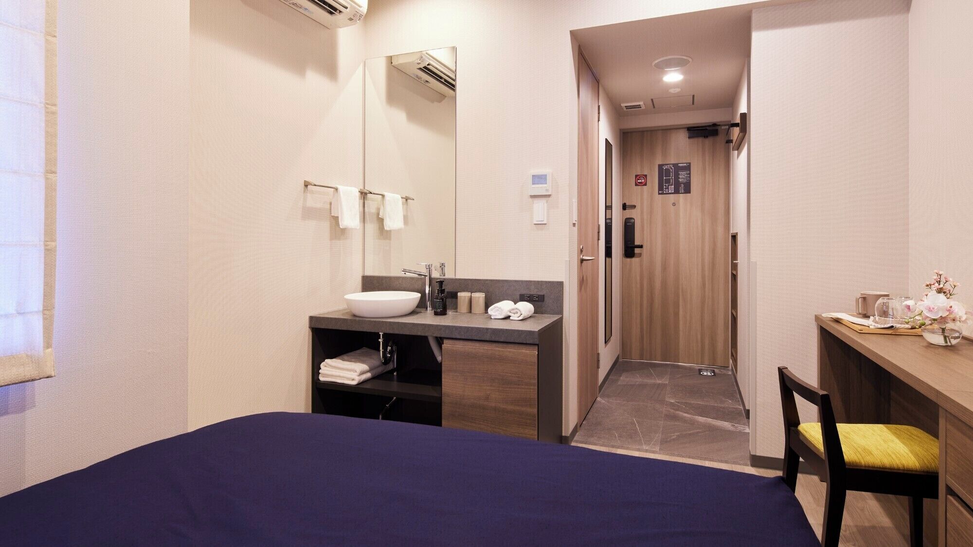 Une chambre d’hôtel moderne comprenant un lit, une salle de bain avec un lavabo et un miroir, ainsi qu’un bureau avec une chaise.