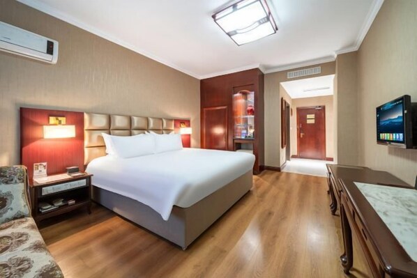 Habitació d'hotel amb llit, taulella de nit, làmpada, televisió i sòl de fusta.