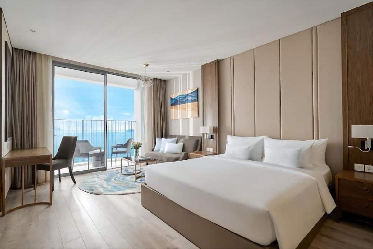 Habitación de hotel con una cama grande, un escritorio, una silla y vistas al mar.