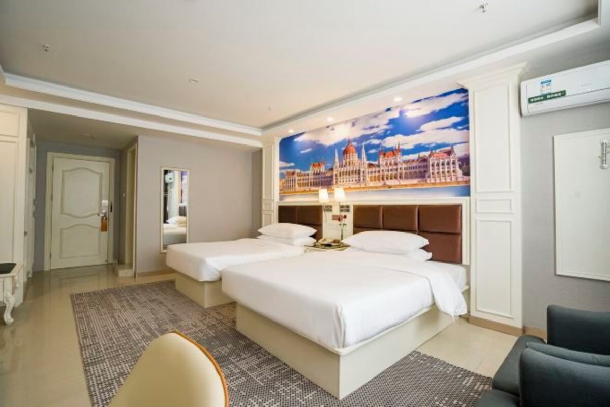 A hotel room with two beds, a large wall mural, a desk, and a chair.