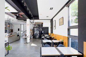 A modern interior with tables and chairs, a kitchen area, and large windows. - Pathway Inn (Penghu)