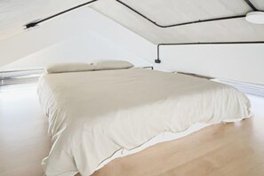 A bedroom with a bed, wooden flooring, and a sloped ceiling with exposed ductwork. - Pathway Inn (Penghu)