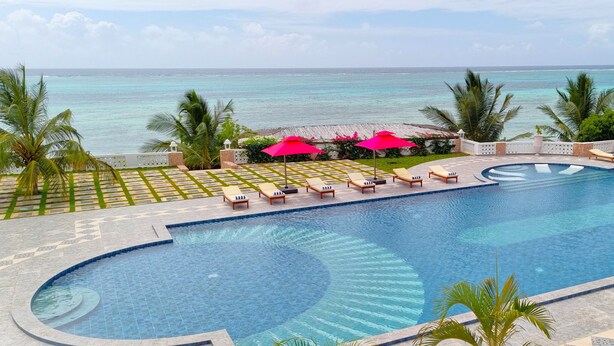 Piscina de un resort con vista al océano, rodeada de palmeras y sillones de descanso.