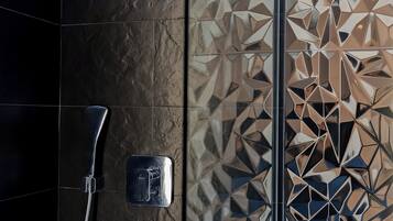 A modern bathroom with a shower, a handheld showerhead, and a glass-enclosed vanity with toiletries.