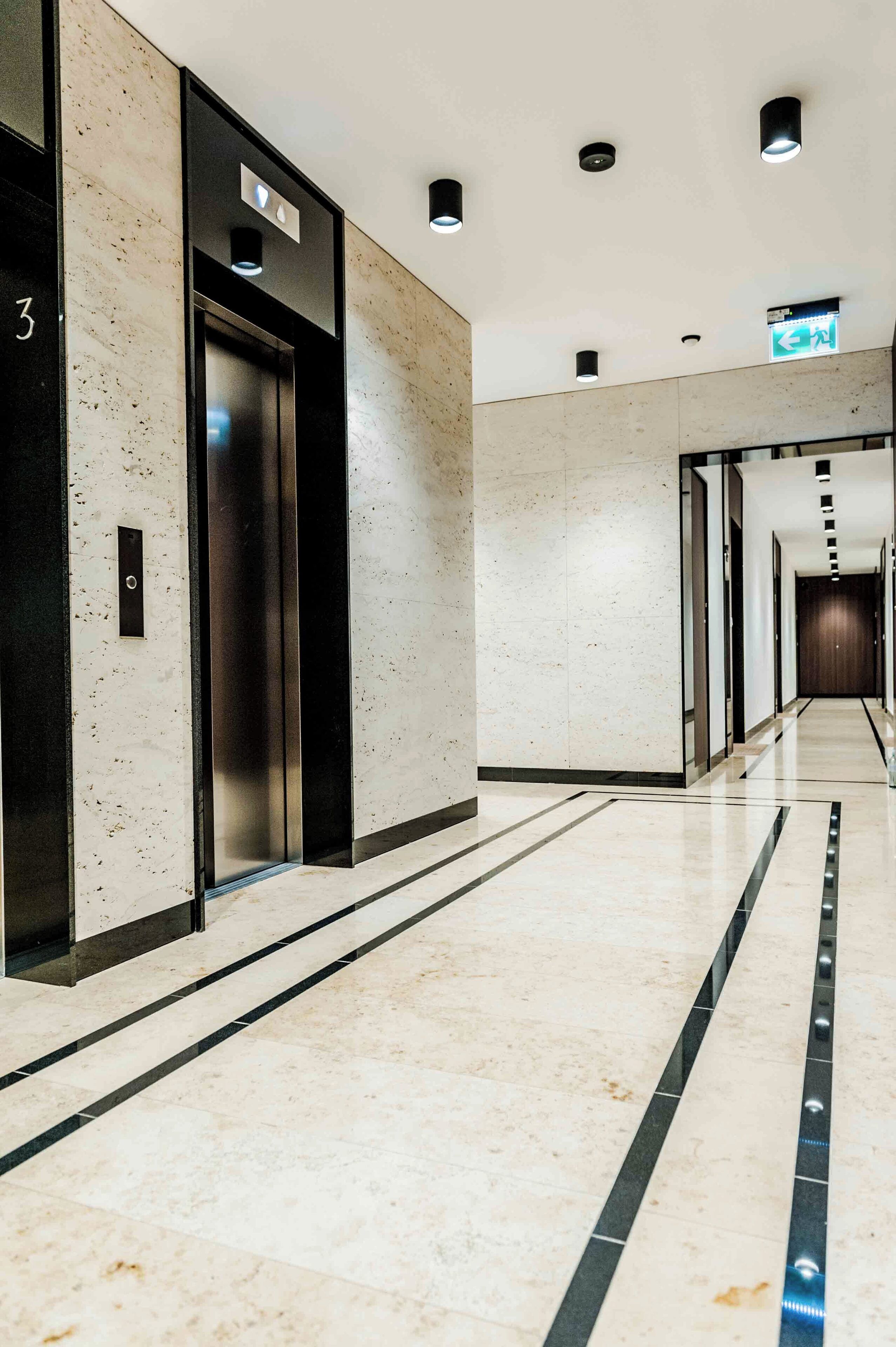 A modern hallway with an elevator, a sign indicating a direction, and a clean, tiled floor.