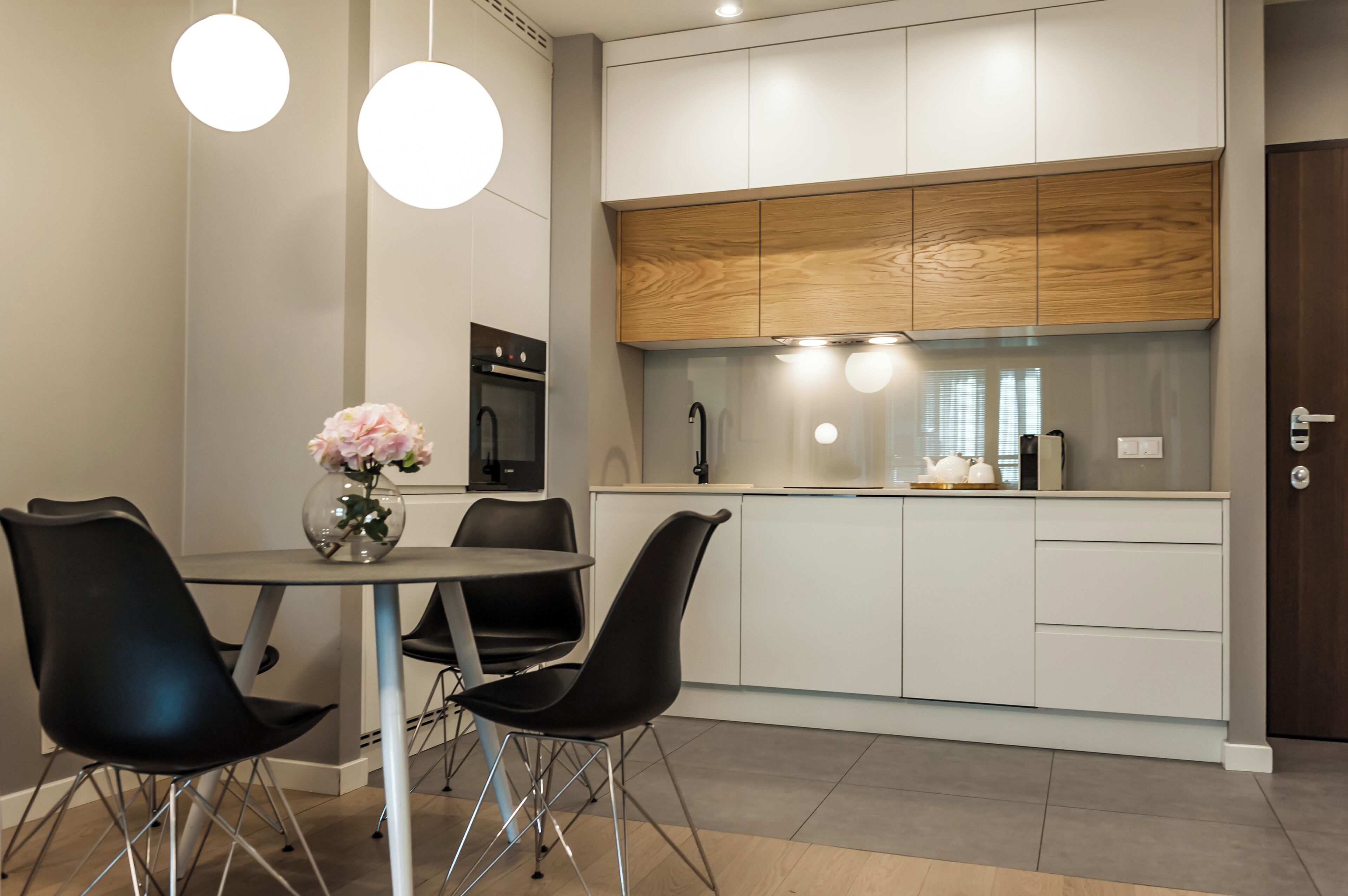 A modern kitchen with white cabinets, a wooden countertop, and black chairs around a round table with a vase of flowers.