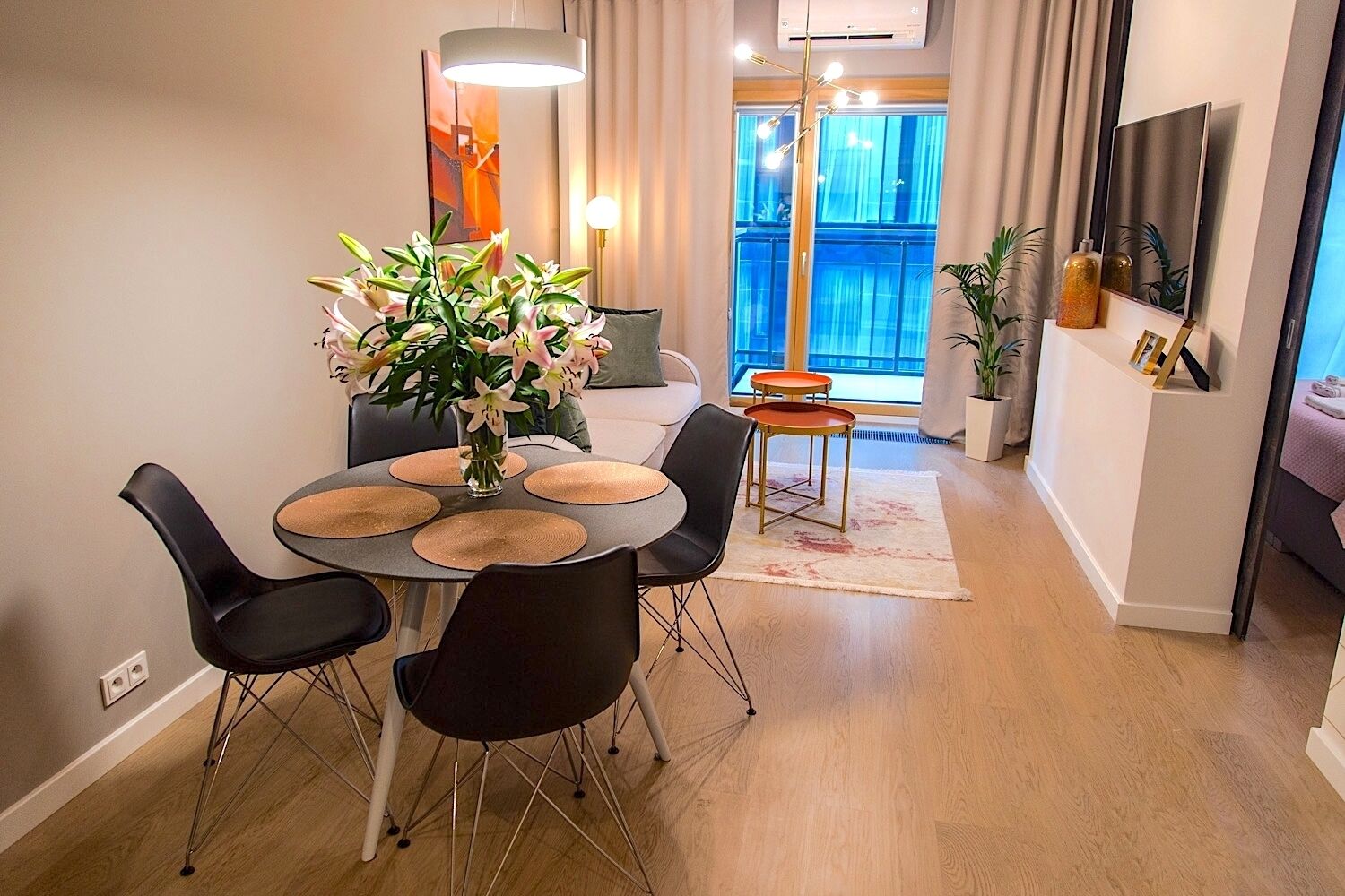 A modern dining area with a round table, black chairs, and a vase of flowers.