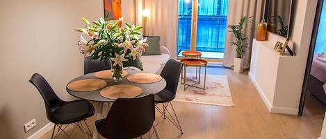 A modern dining area with a round table, black chairs, and a vase of flowers.