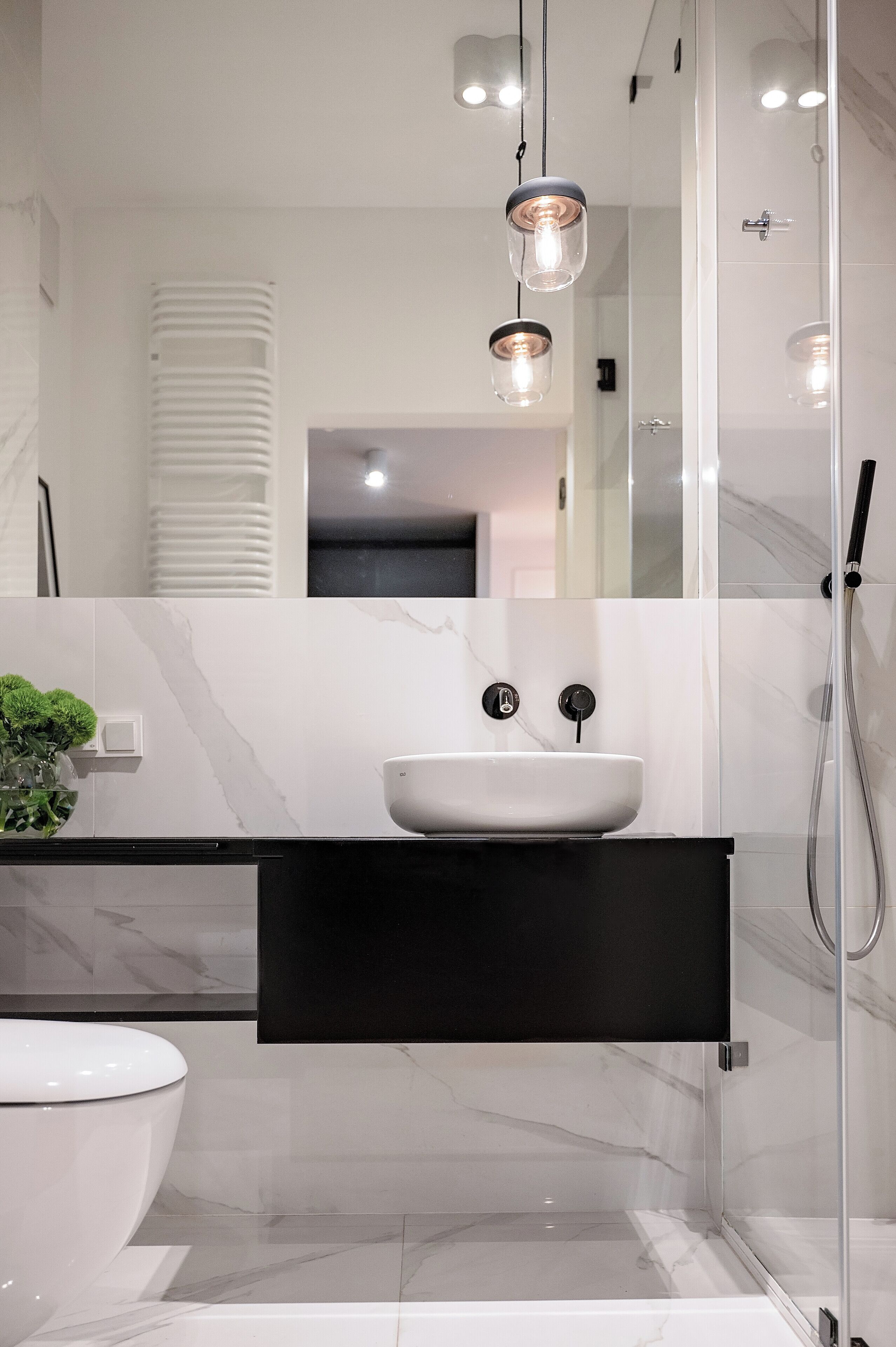 Un baño moderno con un lavamanos blanco, encimera negra y cabina de ducha de vidrio.
