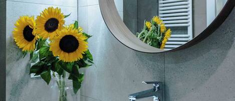 A bathroom with a white sink, a round mirror, and three sunflowers in a vase.