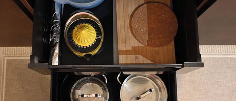 A kitchen drawer with a juicer, a cutting board, and two pots.