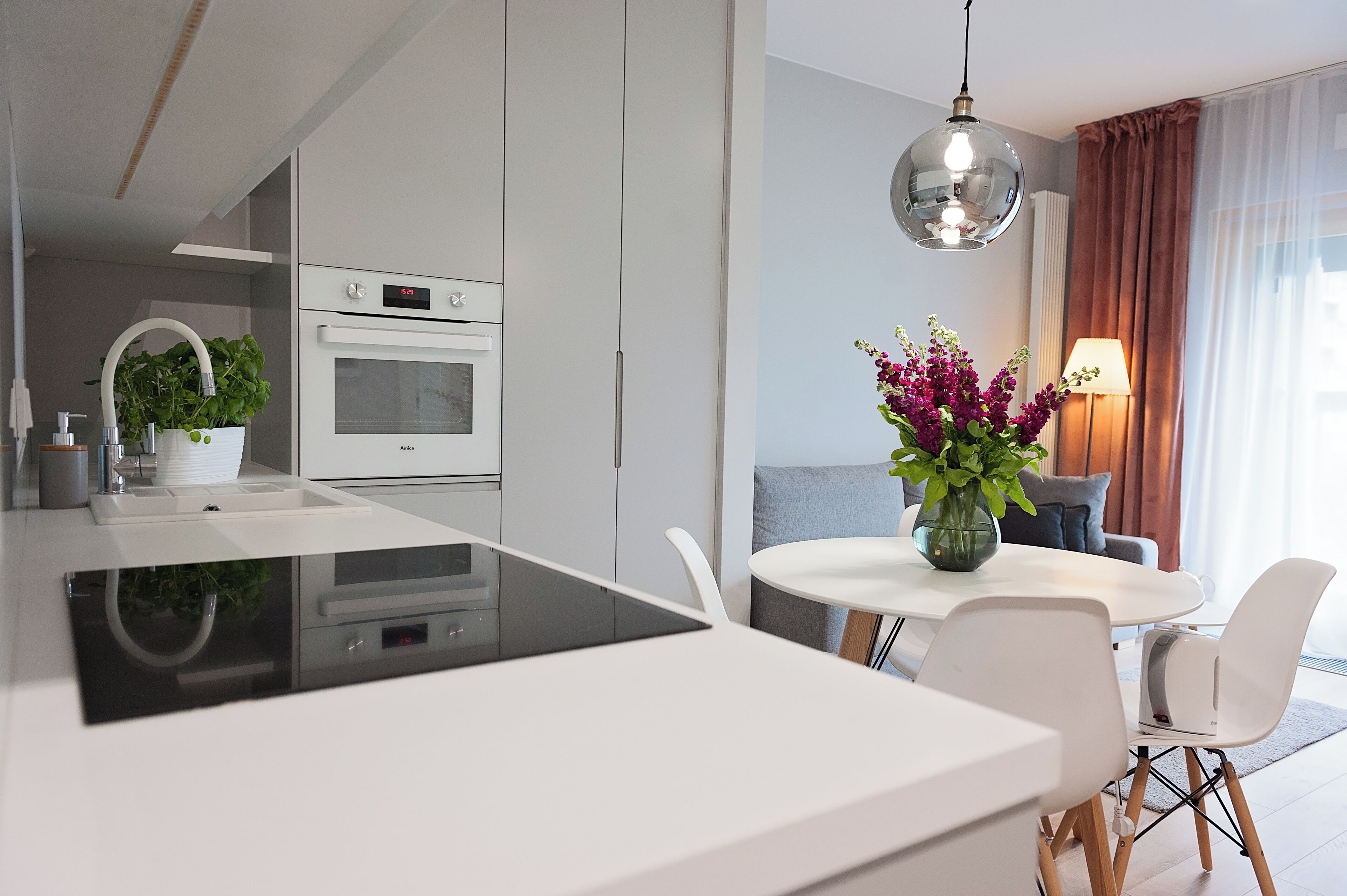 A modern kitchen with white cabinetry, a built-in oven, and a dining area with a white table and chairs.
