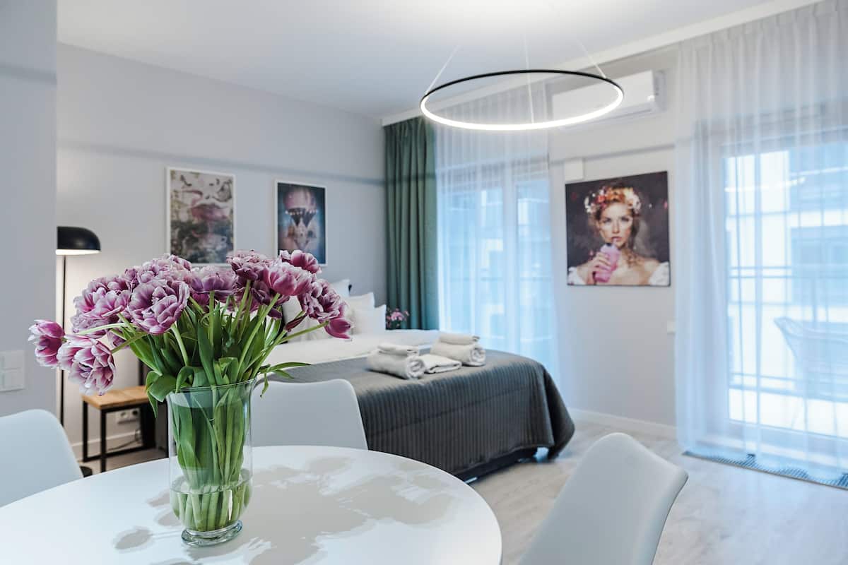 A modern hotel room with a bed, a dining table with a vase of flowers, and artwork on the walls.