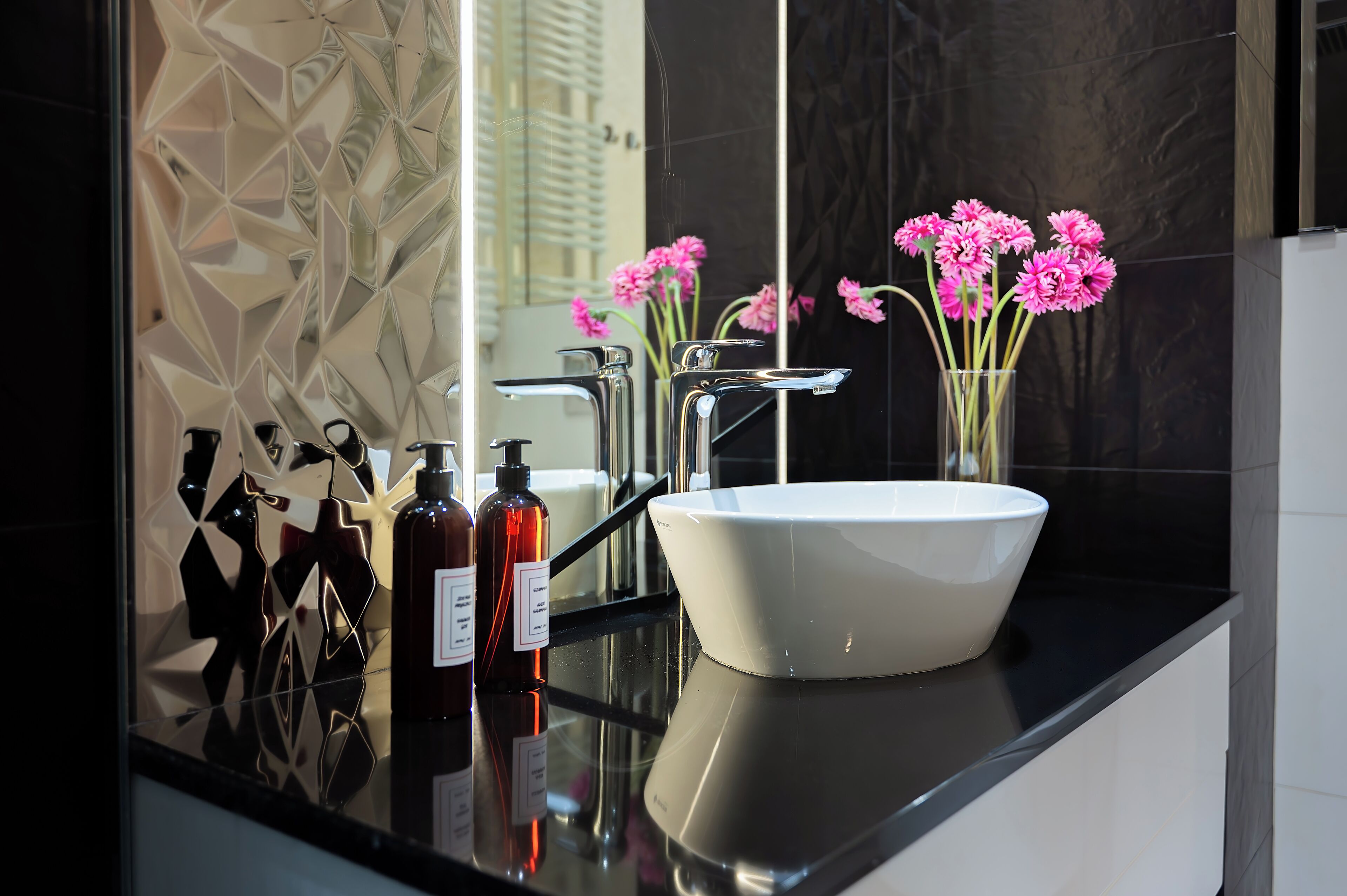 Un baño moderno con un lavamanos blanco, grifos cromados y un florero con flores rosadas en la encimera.