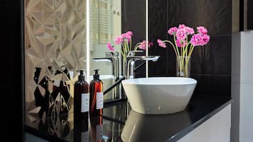 Un baño moderno con un lavamanos blanco, grifos cromados y un florero con flores rosadas en la encimera.